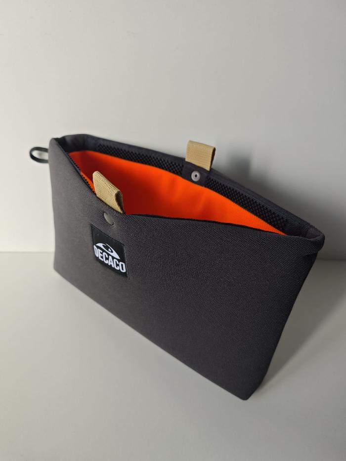  ¡Organiza tus esenciales con estilo! Este práctico neceser combina un exterior elegante en color antracita con un llamativo interior naranja. Su cierre original y su amplio espacio interior lo convierten en el compañero ideal para tus viajes o para mantener tus productos de belleza siempre ordenados.
